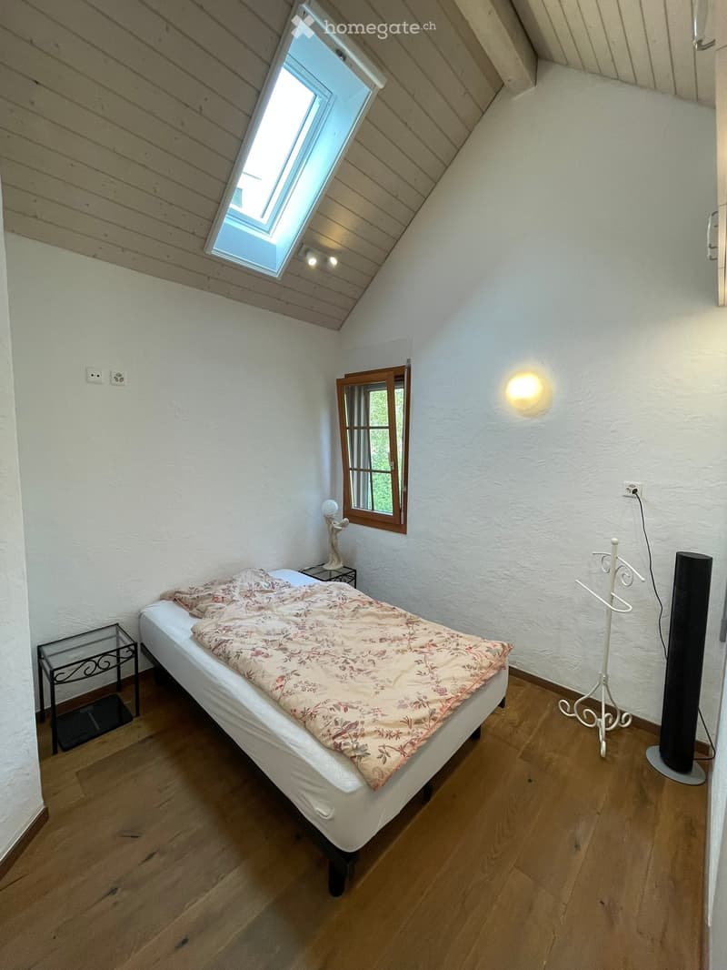 Cozy attic bedroom with wooden floors, white walls, skylight window, and a single bed with floral bedding.