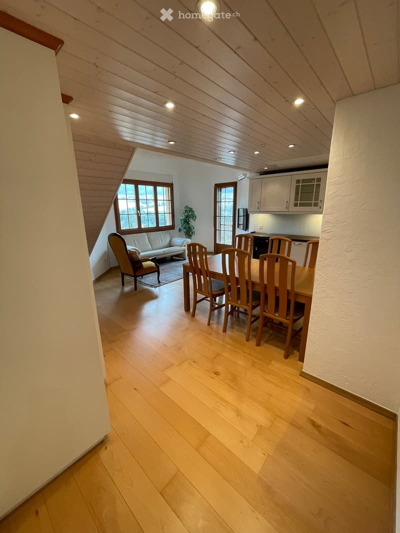 Open-plan living and dining area with wooden flooring, a white sofa, a dining table with chairs, and a small kitchen area with cabinets.
