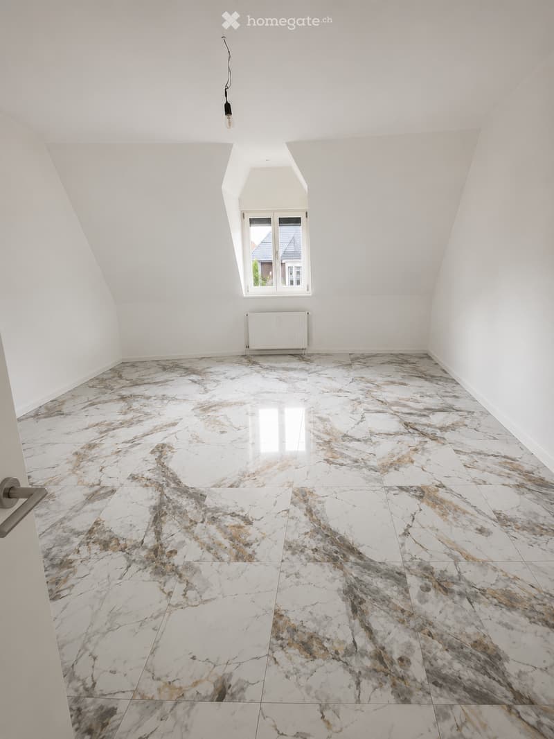 An empty attic room with white walls, a large window, and a marble-patterned floor.