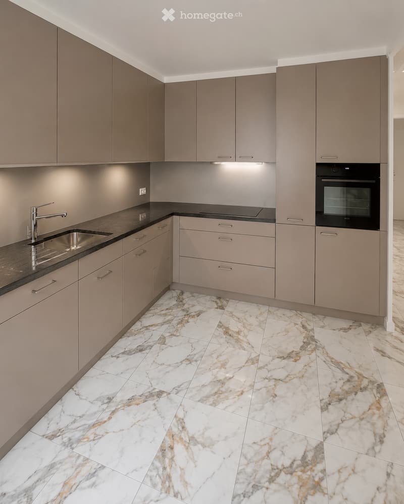 Modern kitchen with light grey cabinets, marble flooring, stainless steel sink, and built-in oven.