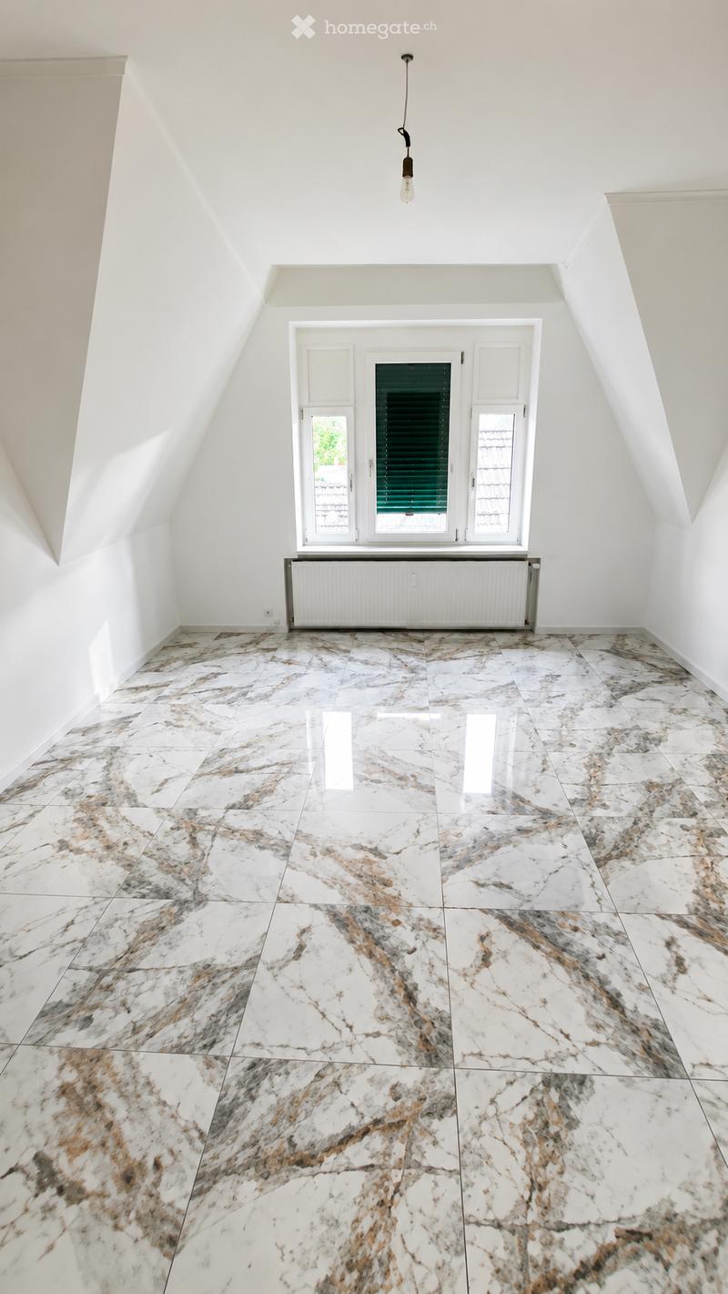 An empty room with white walls, a marble floor, and a large window with shutters. The room features a radiator and a single hanging light fixture.