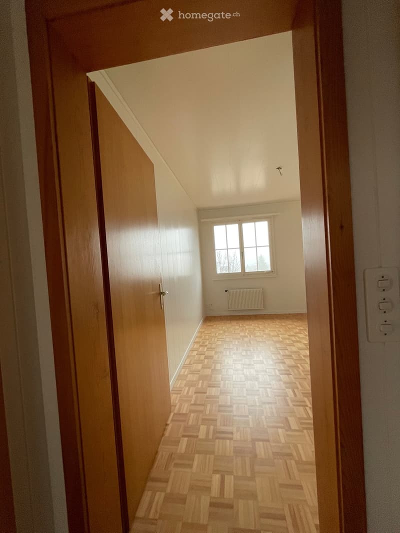 Empty hallway with wooden flooring, white walls, and a window at the end.