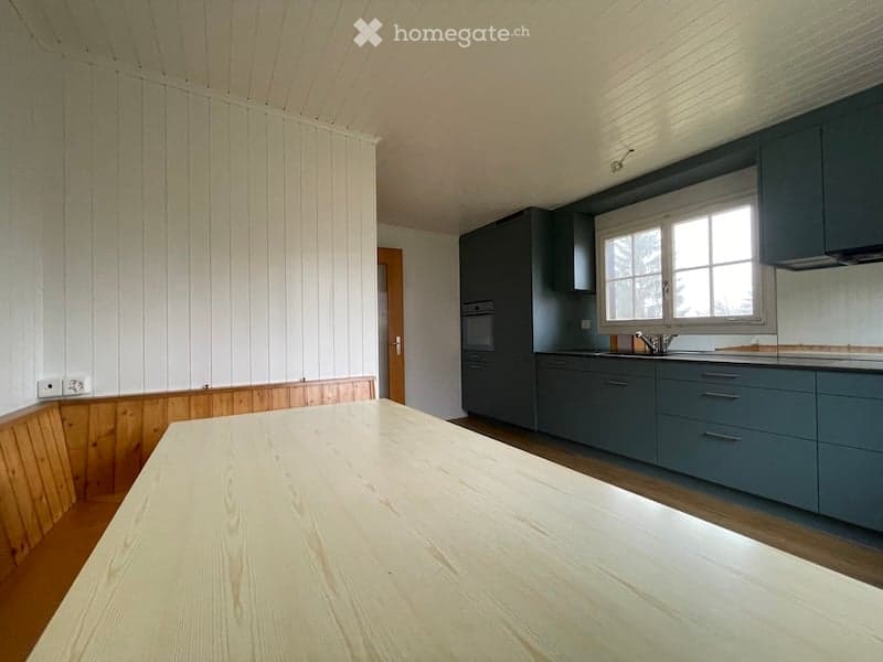 Modern kitchen with grey cabinets, a wooden table, and a sink. The walls are white with wooden paneling on one side.