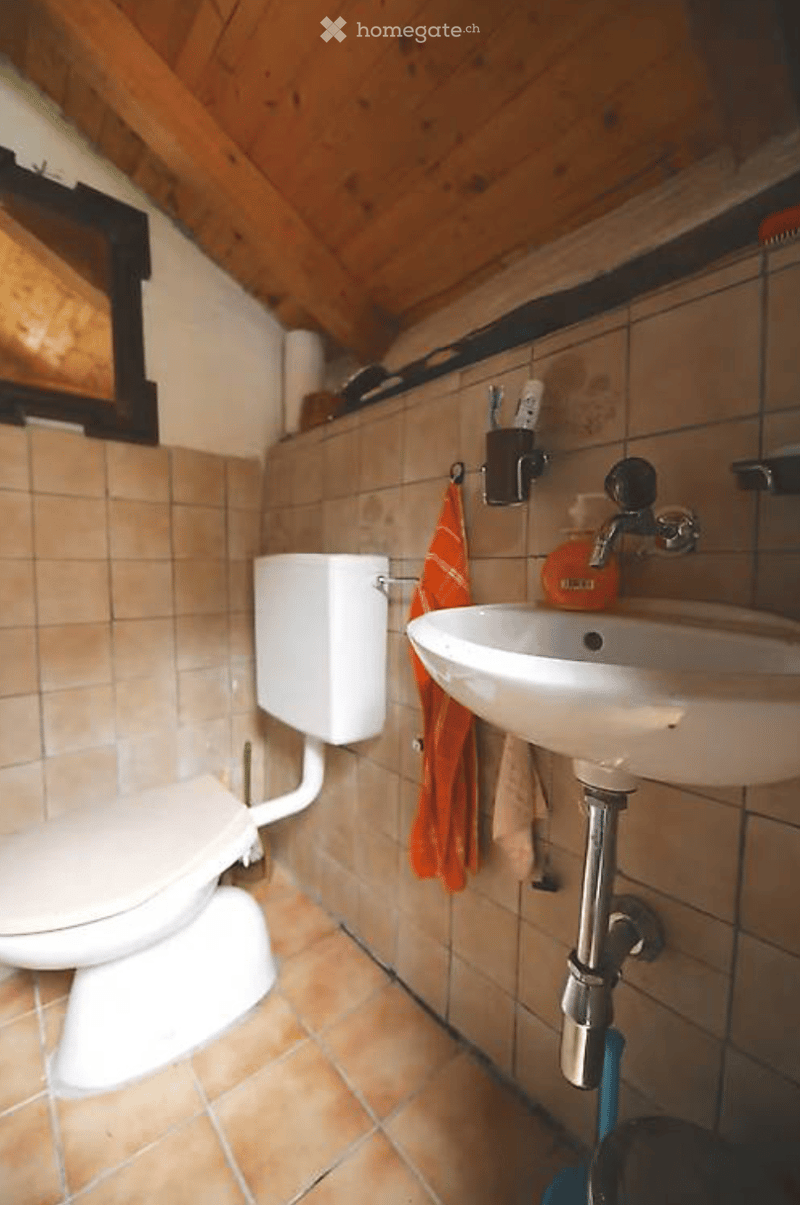 Bathroom with tiled walls and floor, a toilet, a sink with a faucet, a toothbrush holder, and an orange towel hanging on the wall.
