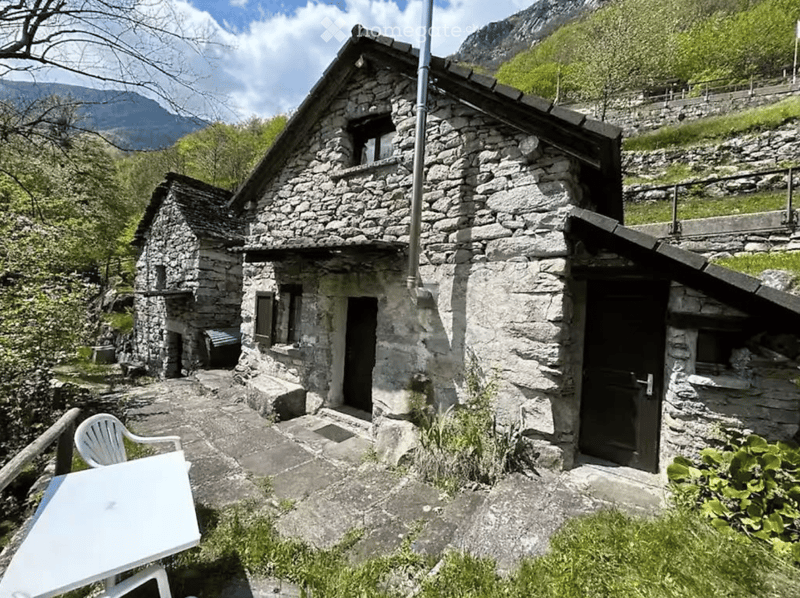 Stone cottage with a rustic design, featuring a slanted roof, small windows, and a stone pathway leading to the entrance.