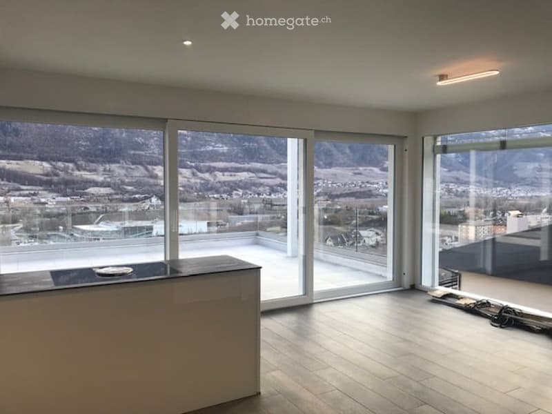 Bright, empty room with large glass sliding doors leading to a balcony, offering a scenic mountain view. The room features a modern design with wooden flooring and minimalistic decor.