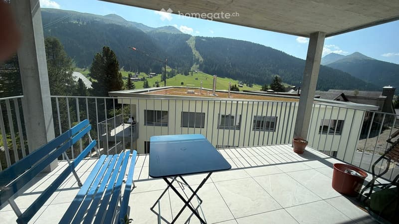 Balcony with a scenic mountain view, featuring a blue bench, a folding table, a chair, and a potted plant.