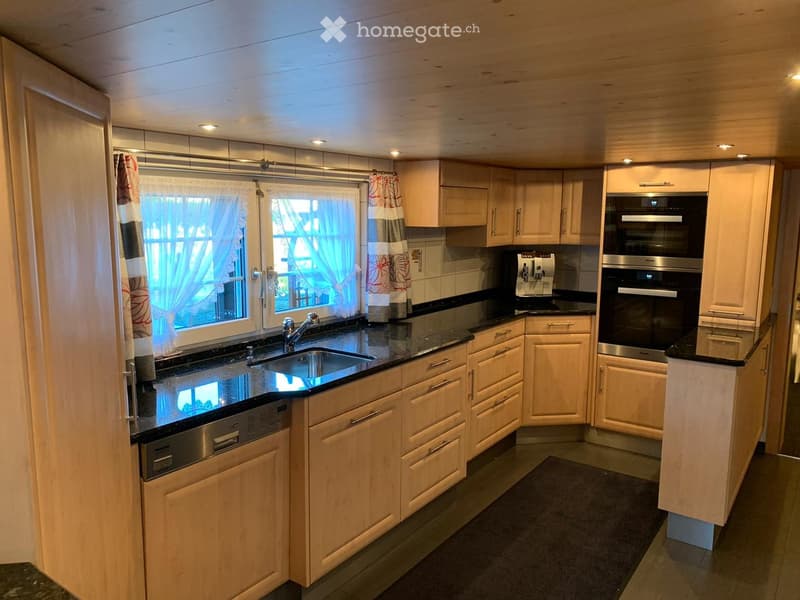 Modern kitchen with light wooden cabinets, black granite countertops, stainless steel appliances, and a window with curtains.