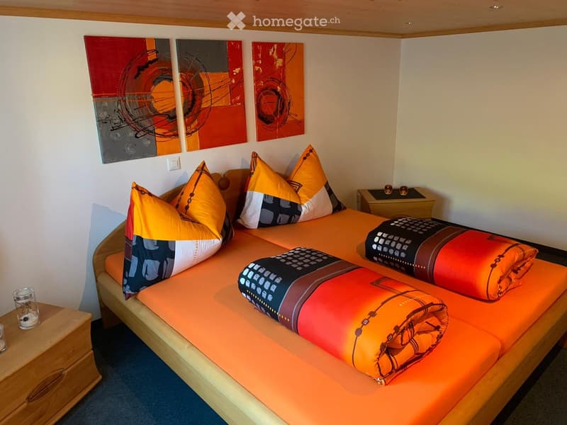 Brightly colored bedroom with a single bed, orange bedding, colorful pillows, and modern artwork on the wall.