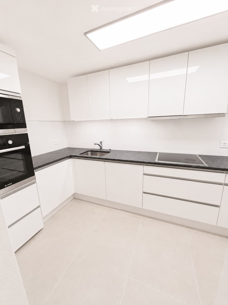 Modern kitchen with white cabinets, black countertop, built-in oven, sink, and faucet. Features a skylight above the sink.