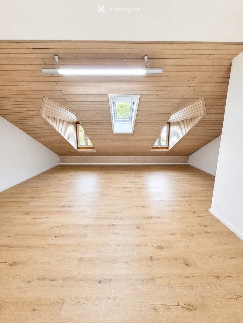 Empty room with wooden flooring and wooden ceiling, featuring skylight windows and recessed lighting.