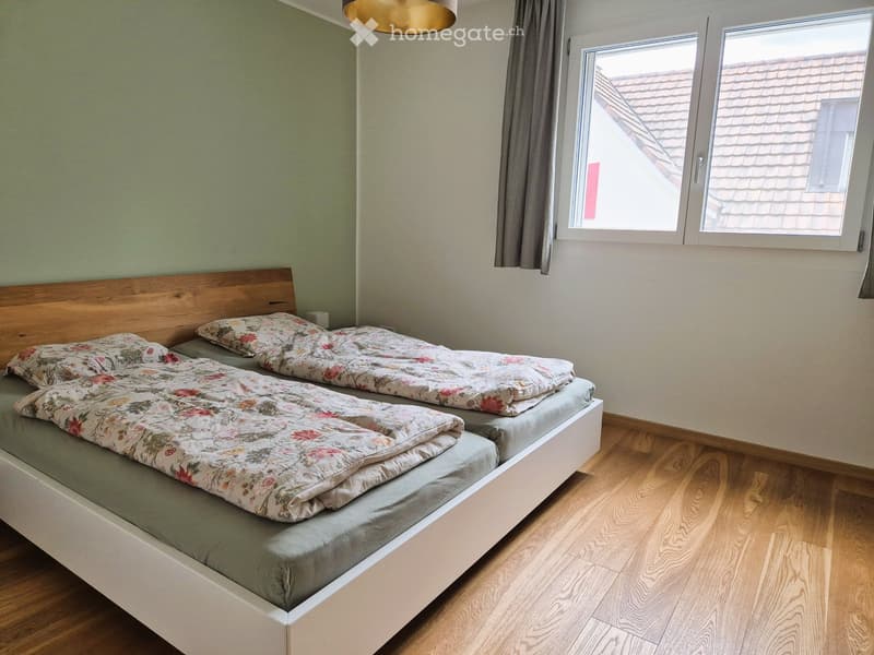 Bedroom with two single beds, wooden flooring, and a window with a curtain.