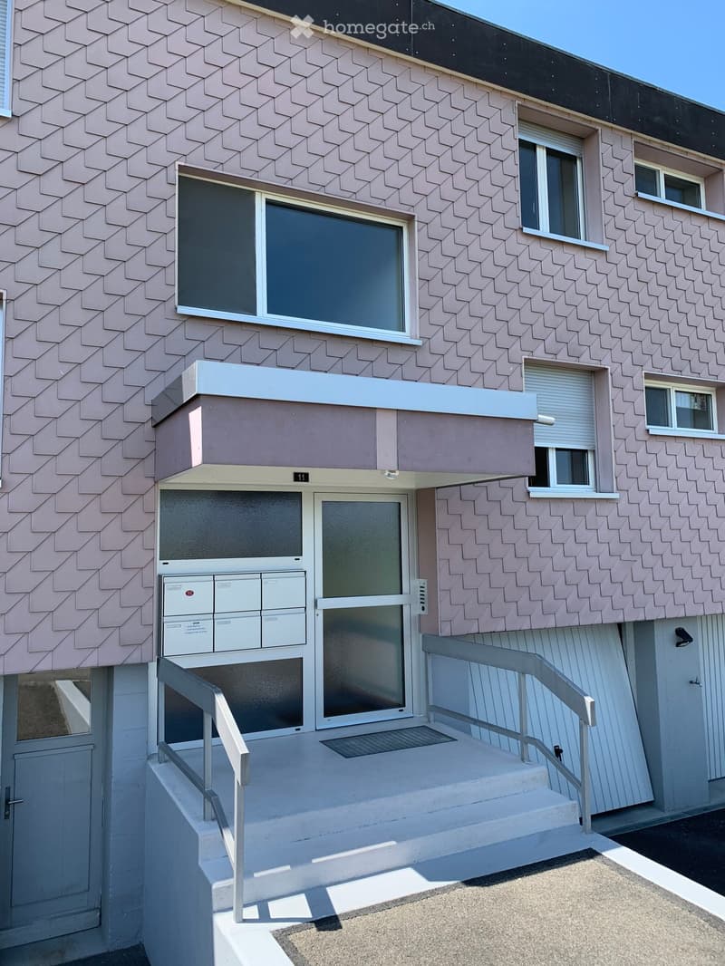Modern multi-story building with pink patterned facade, white-framed windows, and a raised ground floor entrance with stairs and railings.