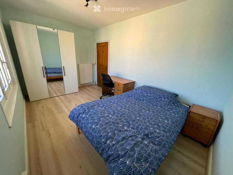 Cozy bedroom with light blue walls, wooden flooring, a single bed with blue patterned bedding, a wooden nightstand, a large mirrored wardrobe, a desk with a chair, and a radiator.
