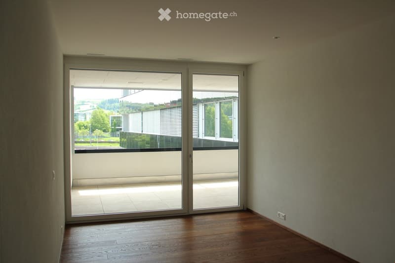 Empty room with wooden flooring, large sliding glass doors leading to a balcony, and light-colored walls.