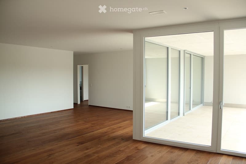 Empty room with wooden flooring, white walls, large glass sliding doors, and a visible adjacent room through an open doorway.