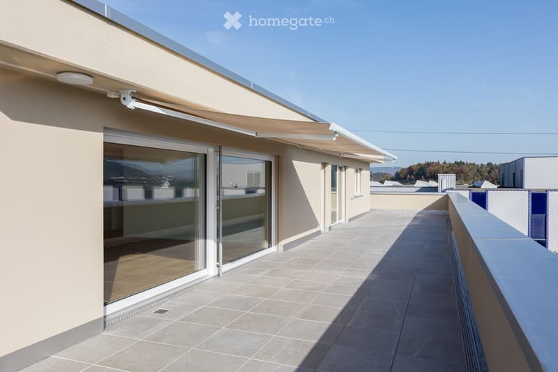 Modern rooftop terrace with tiled flooring, glass sliding doors, and a covered awning extending from the building.