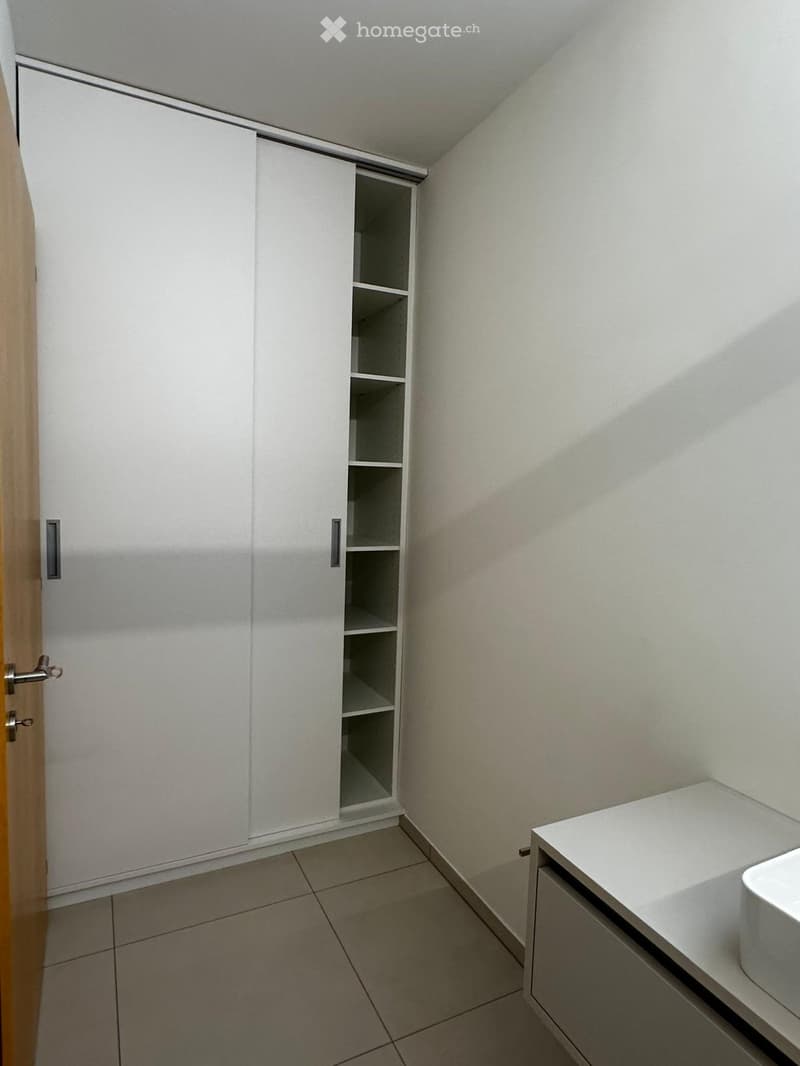 Modern bathroom with white tiled floor, white cabinet, sink, and toilet.