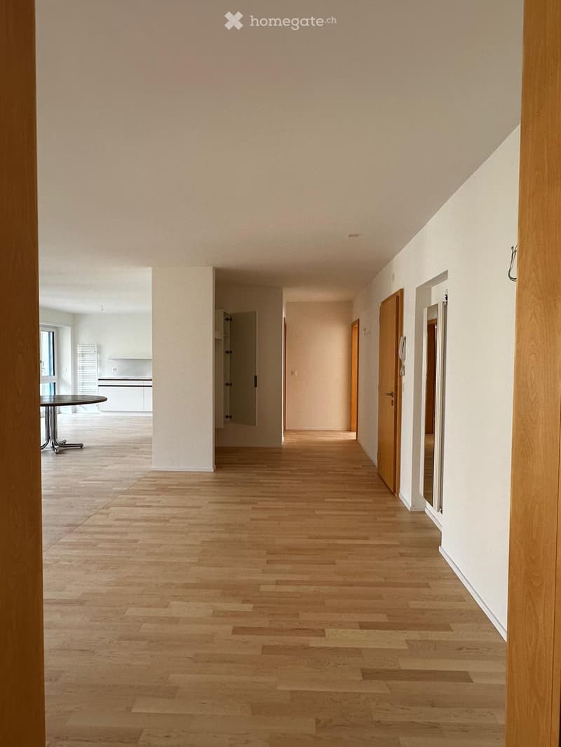 Empty hallway with light wooden flooring, white walls, and several doors leading to other rooms.