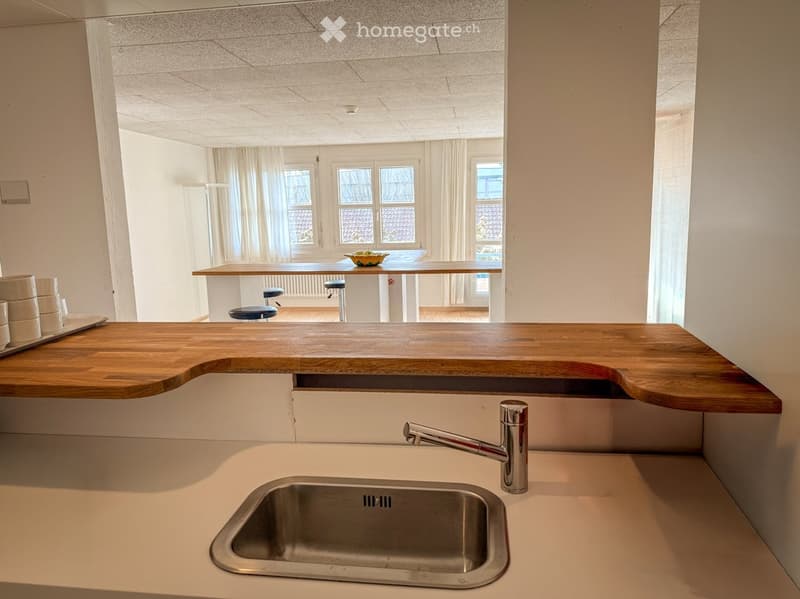 Modern kitchen with a wooden countertop, stainless steel sink, and a small dining area with stools and a table.