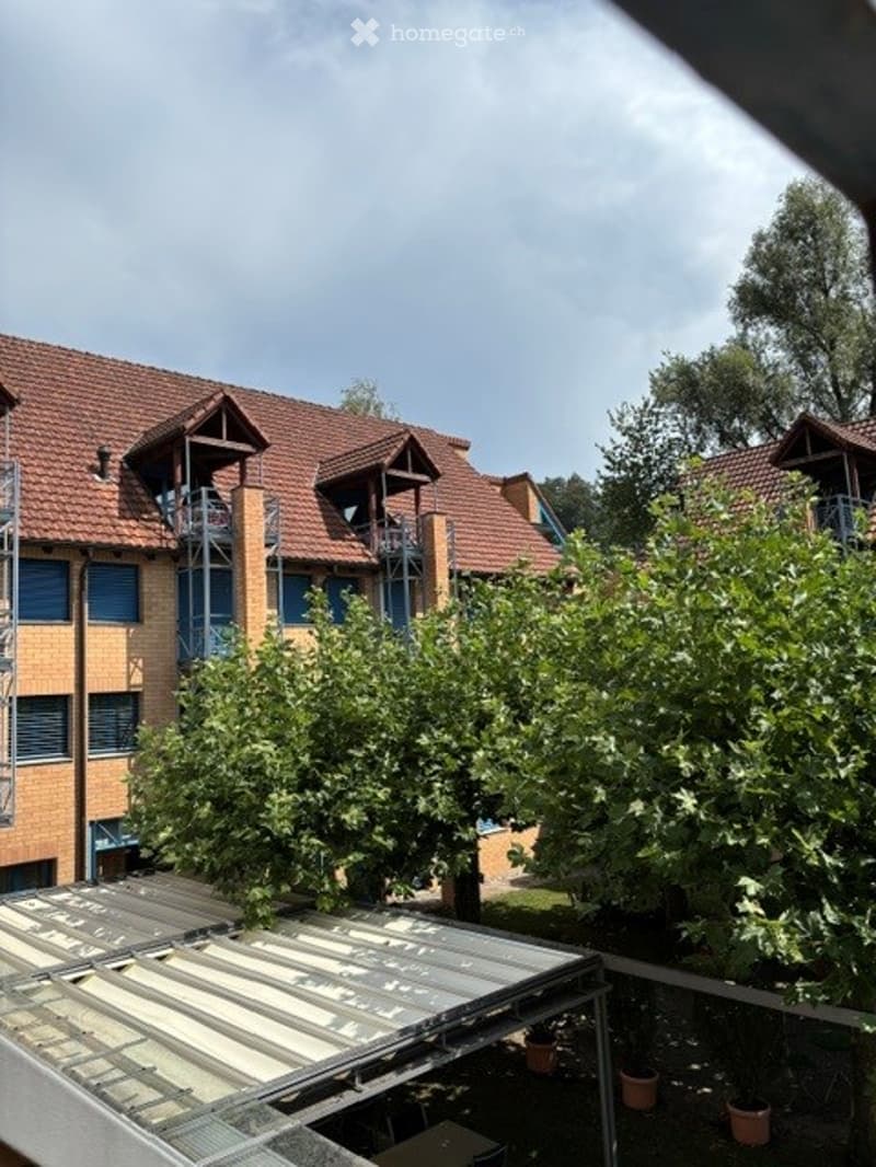 Multi-story residential building with red-tiled roof, balconies, and surrounding greenery.