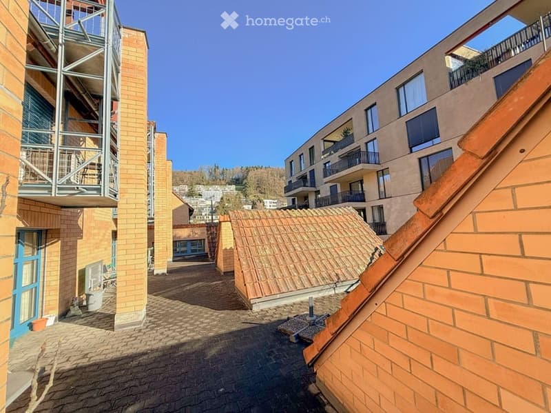 Courtyard view of a residential complex with brick buildings, balconies, and a clear blue sky.