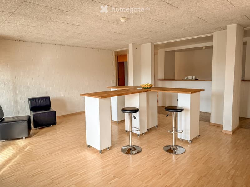 Modern, minimalist room with a wooden bar counter, two black leather sofas, and two black bar stools. The floor is light wood, and the walls are white.