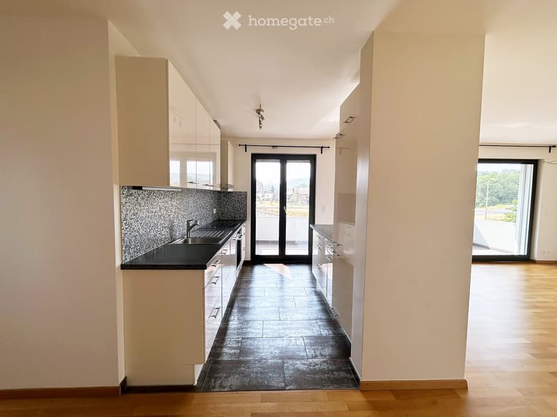 Modern kitchen with white cabinets, black countertop, and dark tiled floor. Features a sink with a faucet, and large sliding glass doors leading to a balcony.