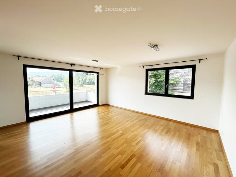 Empty room with wooden flooring, large sliding glass door, and a window with black frame. No furniture or equipment present.