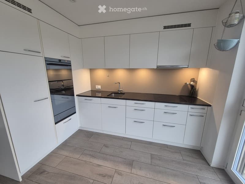 Modern kitchen with white cabinets, black countertop, and stainless steel appliances including an oven and sink.