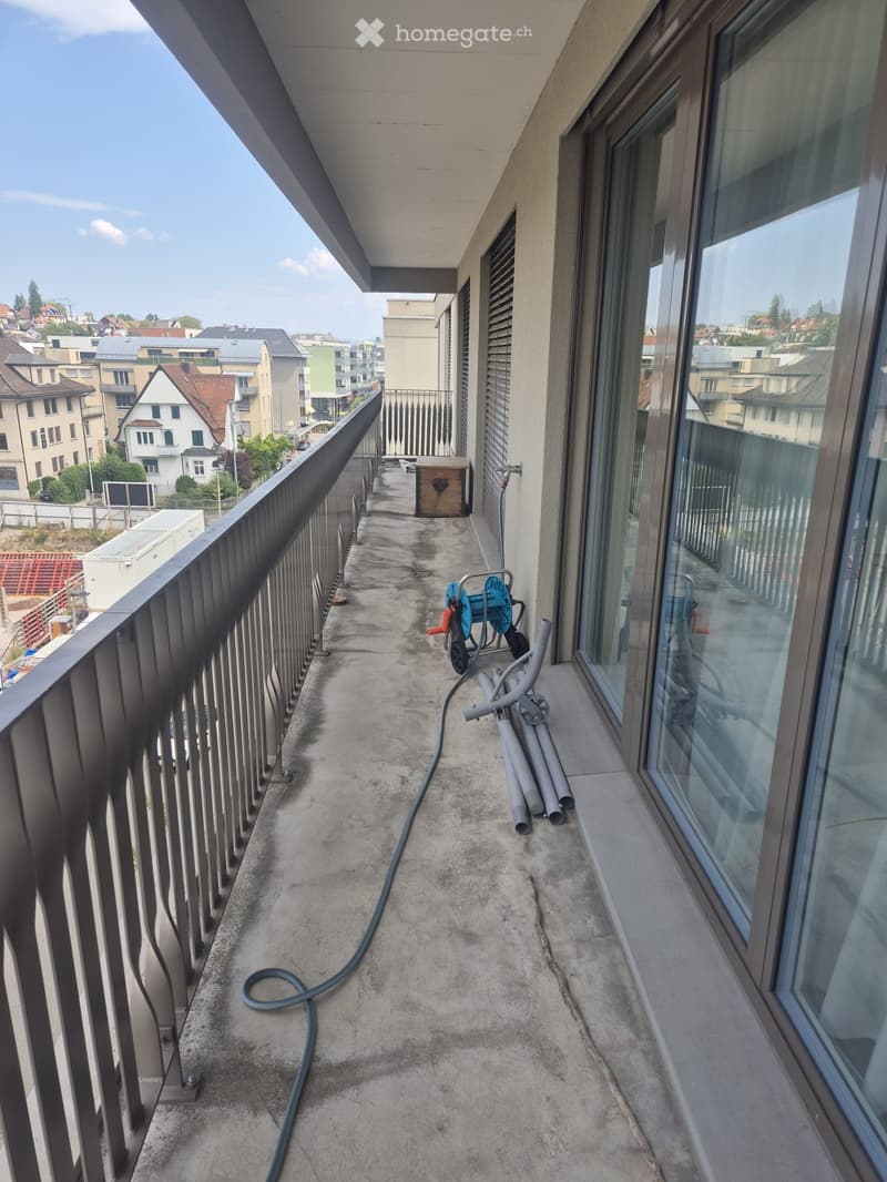 Balcony with metal railing, concrete floor, large windows, and a view of the city.