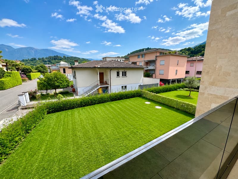 Well-maintained lawn with trimmed hedges, surrounded by residential houses and trees, with a scenic mountain backdrop.