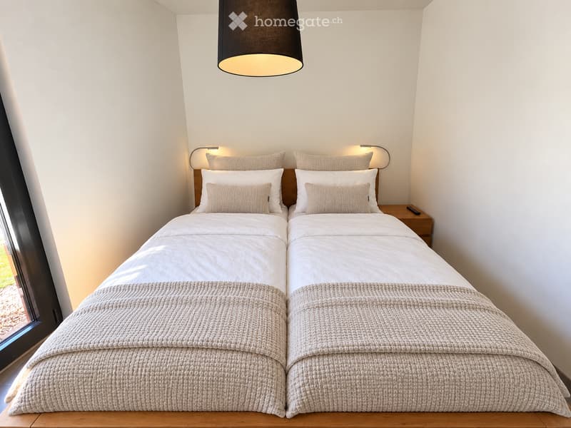 Modern bedroom with two single beds, beige bedding, nightstand, and pendant light.