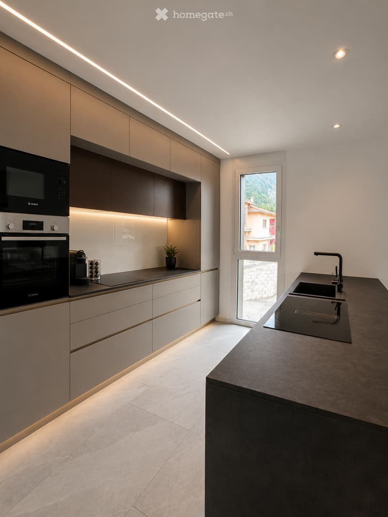 Modern kitchen with sleek, light-colored cabinets, a dark countertop, built-in oven, and a sink with a modern faucet. A small plant sits on the counter, and the space features integrated LED lighting along the cabinets and ceiling.