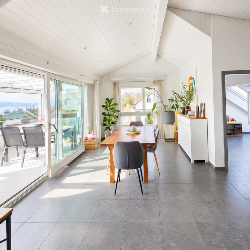 Bright dining area with a wooden table, six chairs, a cabinet, and large windows offering a scenic view.