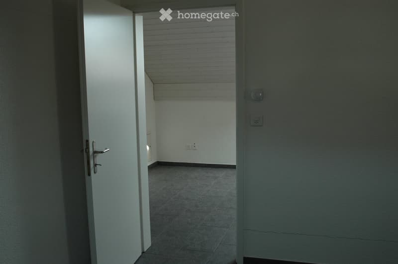 Empty room with tiled floor, white walls, and a partially open door leading to another space.