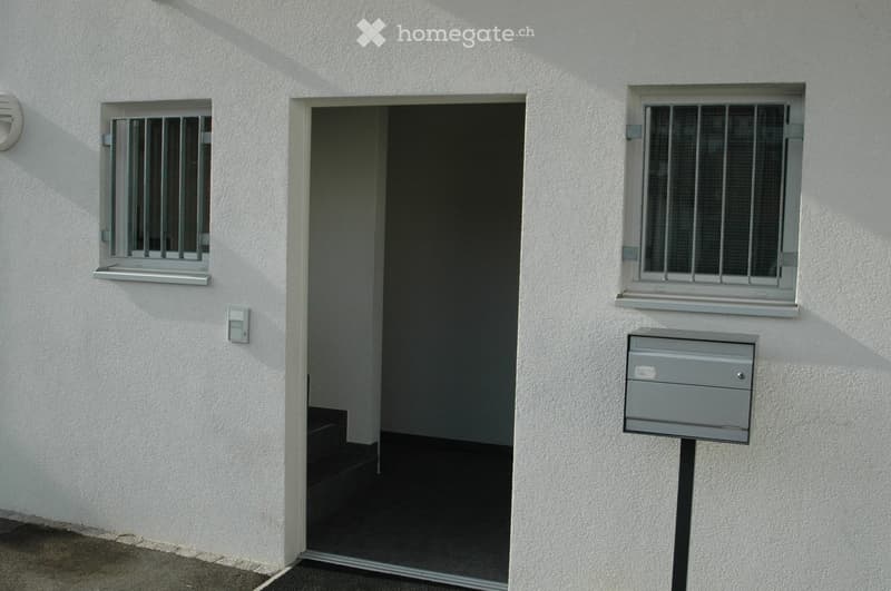 White building exterior with a raised ground floor entrance, two barred windows, and a mailbox.