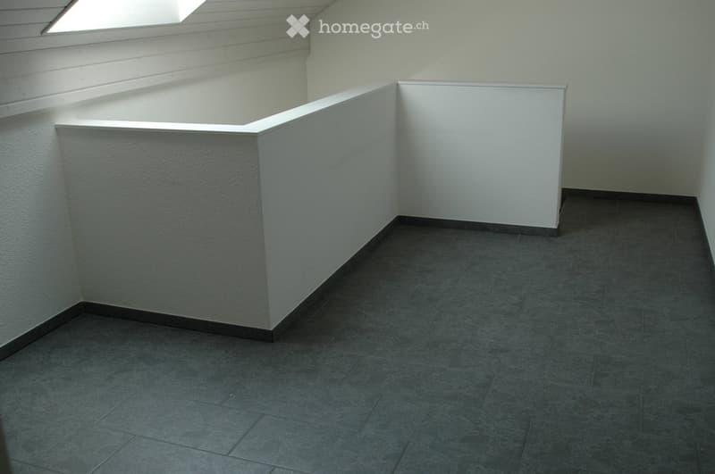 Empty room with grey tiled floor and white walls, featuring a raised platform area with a skylight above.