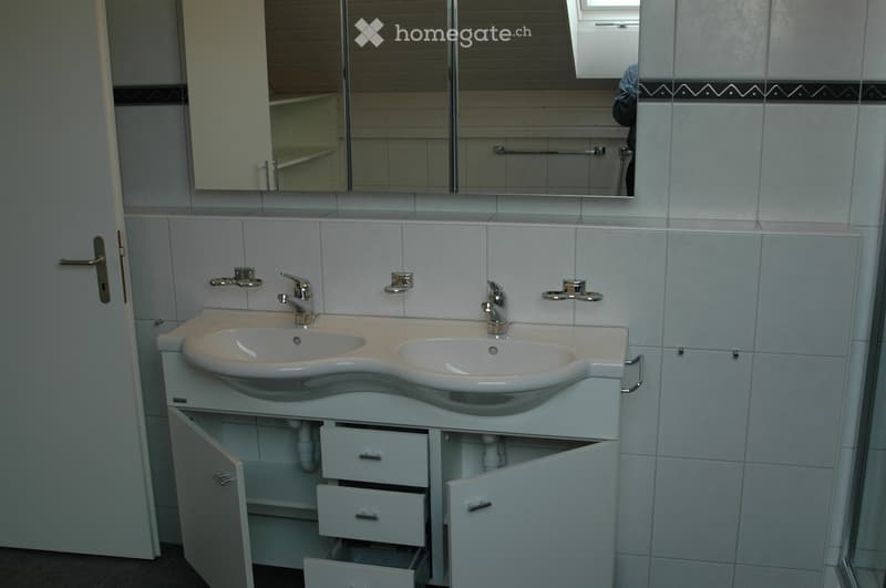 Modern bathroom with a double sink vanity, two faucets, mirrored cabinet, and tiled walls.