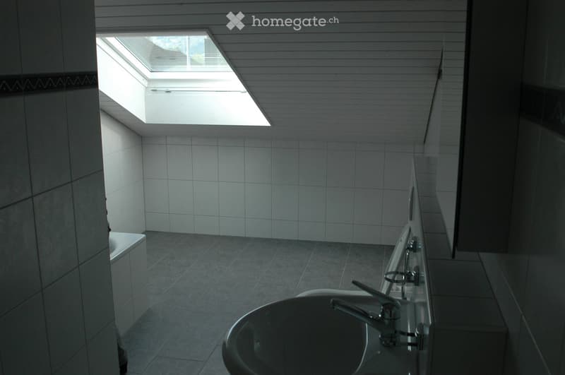 Modern bathroom with white tiled walls and floor, a large skylight window, and a sleek sink with a modern faucet.