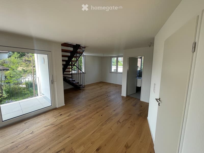 Empty room with wooden flooring, white walls, large sliding glass door leading to a balcony, and a staircase leading to another level.