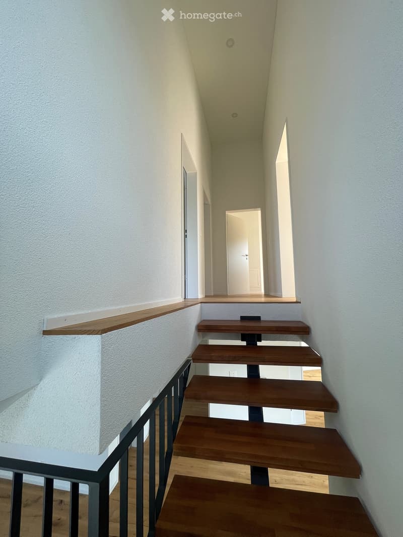 Modern staircase with wooden steps and a metal railing, leading to an open doorway at the top.