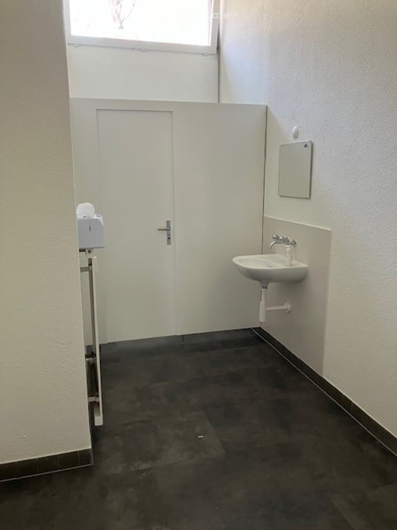 small room with white walls, black floor, white door, sink, mirror, and tissue holder