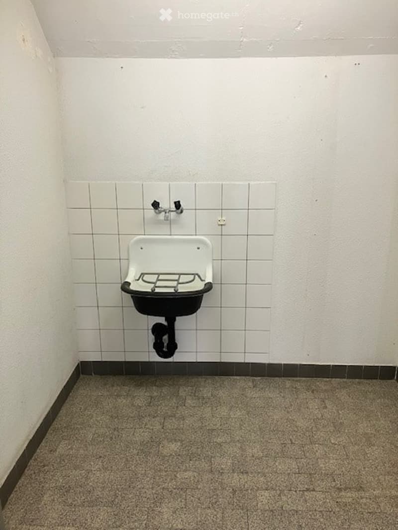 A small room with a sink mounted on the wall, white tiled walls, and a tiled floor.