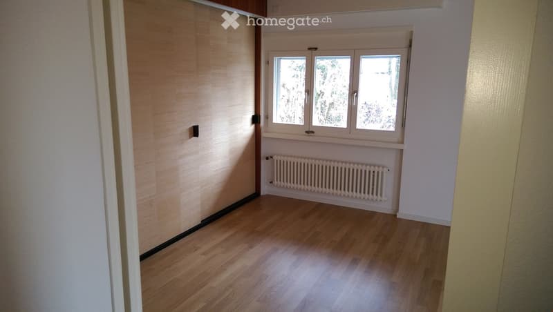 Empty room with wooden flooring, white walls, and a window with three panes. A radiator is placed below the window.