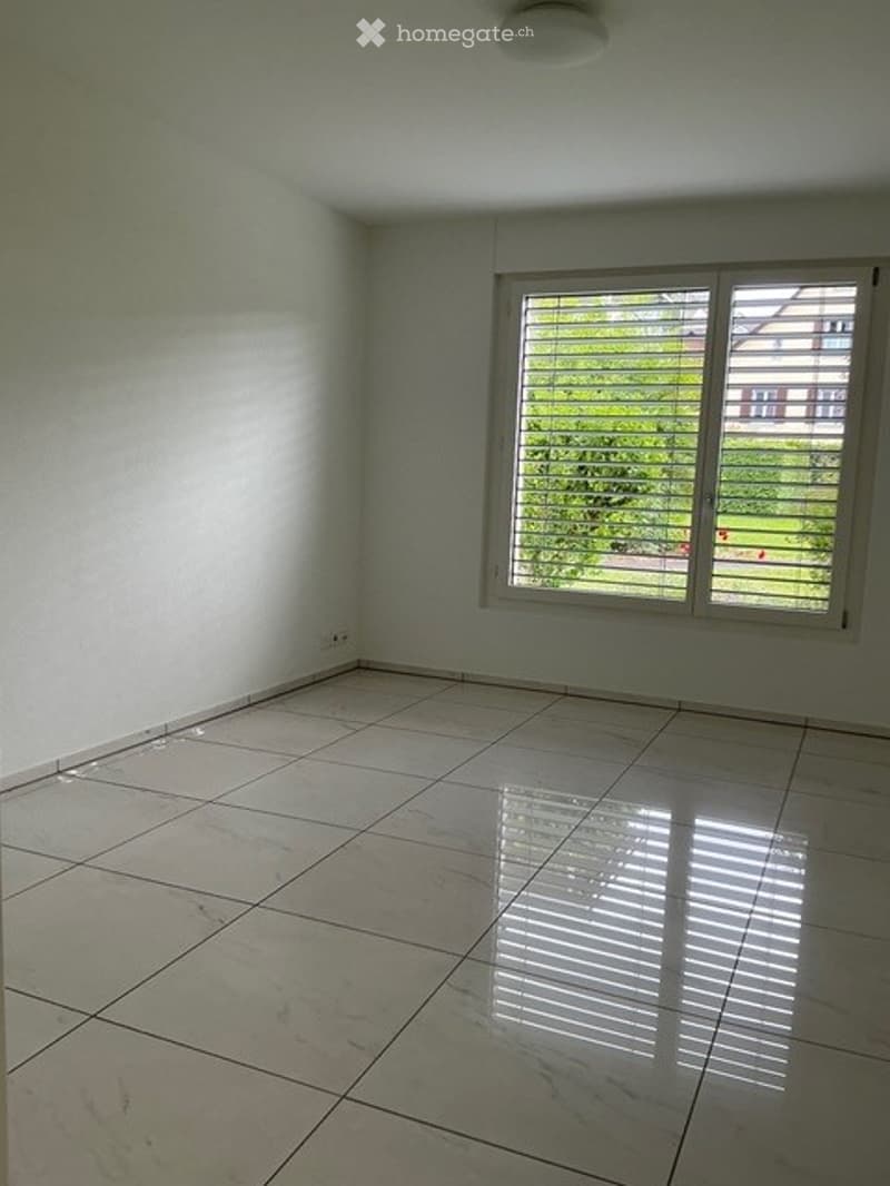 Empty room with white walls, tiled floor, and a large window with blinds. No furniture or equipment present.