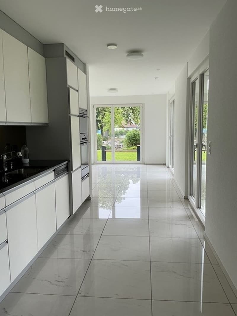 Bright, modern hallway with white walls, polished tile flooring, and large glass doors leading to a garden view.