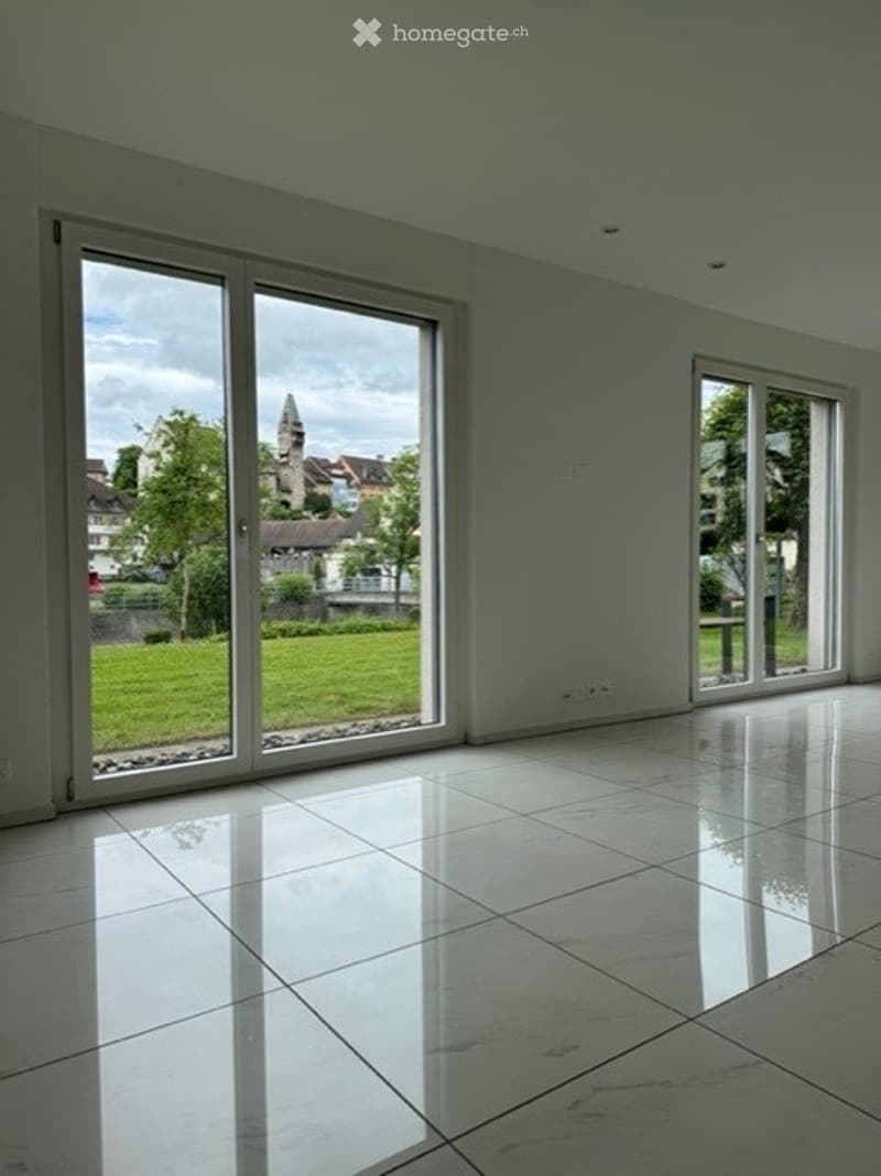 Empty room with large sliding glass doors, white tiled floor, and natural light from the windows.