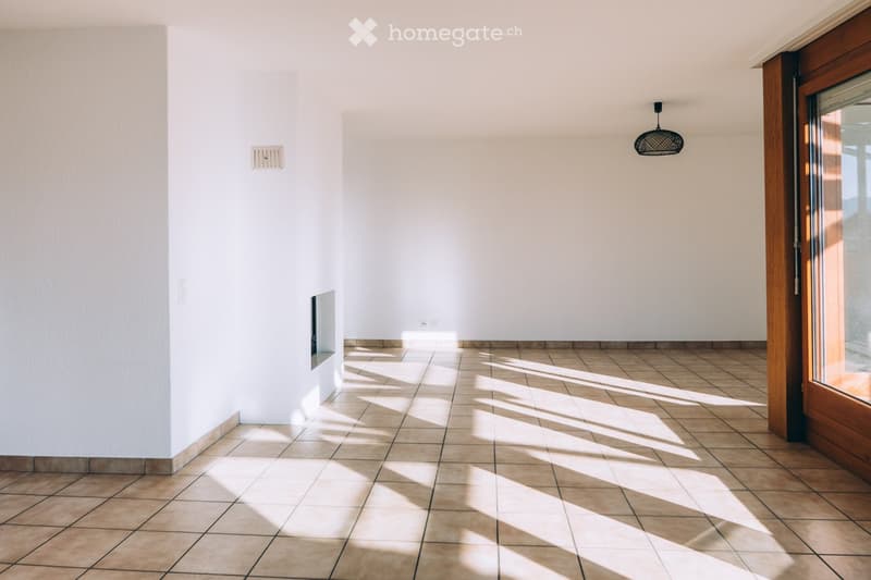 Empty room with tiled floor and white walls, featuring a hanging light fixture and a wooden door with glass panels.