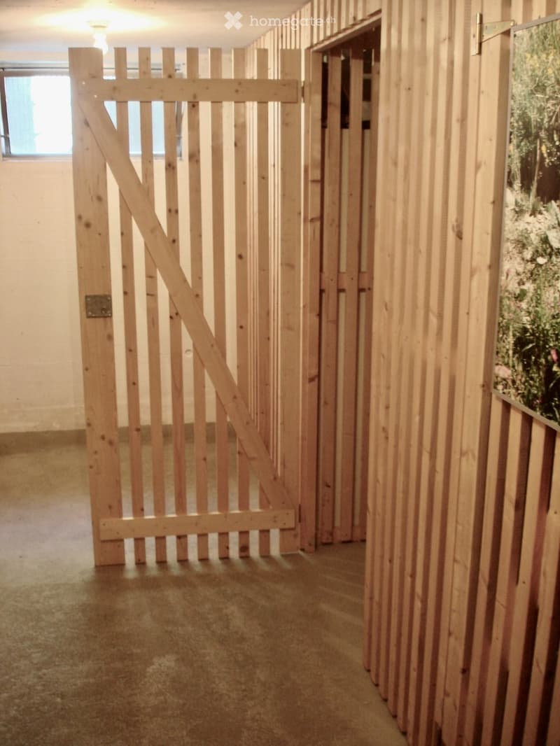 Empty hallway with wooden panel walls, a large wooden gate, and a small window letting in natural light.